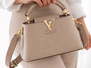 louis-vuitton-beige-leather-top-handle-handbag-held-by-woman-with-gold-lv-logo-white-background